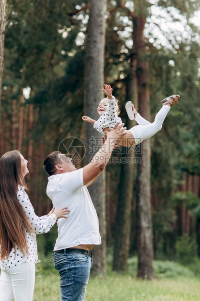 父亲在暑假时吐出孩子的自然父亲在暑假时将孩子抛出母亲父和女孩在夏季公园玩耍女孩飞行友好家庭的概念选择焦点图片