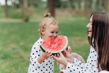 快乐的母亲和女儿在夏季公园吃西瓜快乐的笑脸家庭在公园吃西瓜母亲和女儿一起度过时间饮食维生素健康的食物概念选择焦点饮食健康的物概念图片