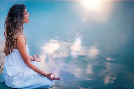 在湖边做瑜伽的年轻美女坐在莲花的姿势上图片