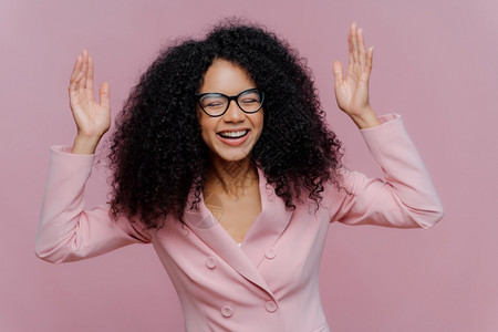 情绪激动的女企业家举手真诚笑佩戴眼镜和正式夹克在商业领域工作在室内穿紫色背景布置快乐的情感概念图片