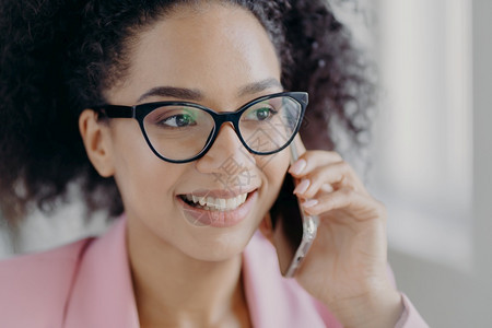 美丽的笑脸黑皮肤女人的头部戴着光眼镜拥有现代手机精心照顾的外衣谈论未来的投资与商业伙伴抛开图片