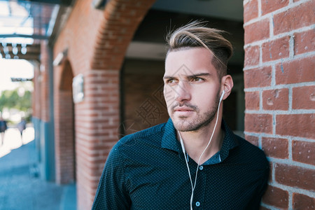 英俊的年轻男子在街上用耳机听音乐的肖像城市概念图片