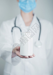 戴蓝色面罩的医生以疗面罩持有灰色医院墙底的塑料药箱抗生素维他命和治疗药片图片