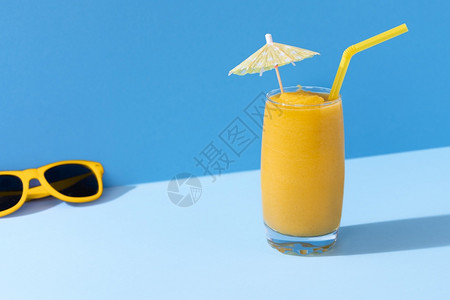 蓝色背景的芒果冰淇淋和黄色太阳镜严酷的光明媚的夏日风景热带的冰雪芒果鸡尾酒背景图片