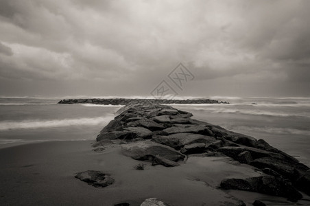黑白的海滩上断水石黑暗的暴风天空和意大利拉齐奥的海浪图片