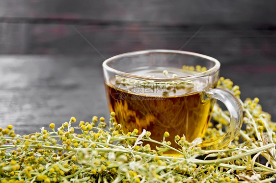 玻璃杯中的灰色蠕虫树草药茶木板背景上的鲜树枝花图片