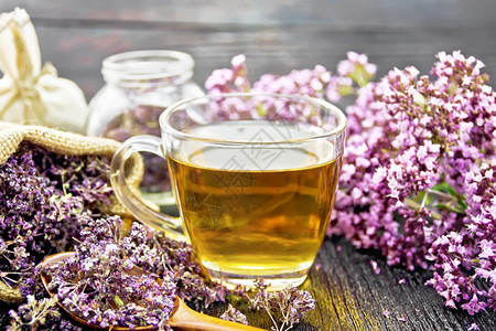 玻璃杯中的红树草药茶鲜花袋子中的干马约兰花木板底的罐子和勺图片