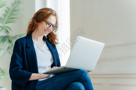 职业女雇主享有工作程序用笔记本电脑设备坐在双腿交叉线聊天有正面的外观红卷发穿时尚优雅的衣服图片