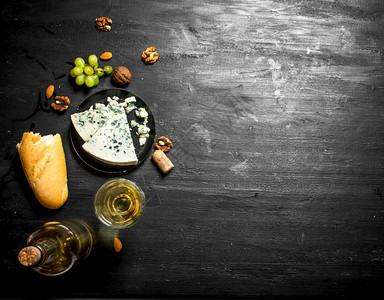 白葡萄酒加法国蓝奶酪和坚果黑木板上图片