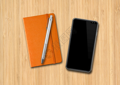 木制桌上的闭橙笔和智能手机笔和智能手机放在木制桌上图片
