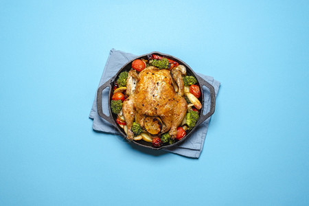 用铁铸的烤鸡和蔬菜在蓝色背景的视图上方背景图片