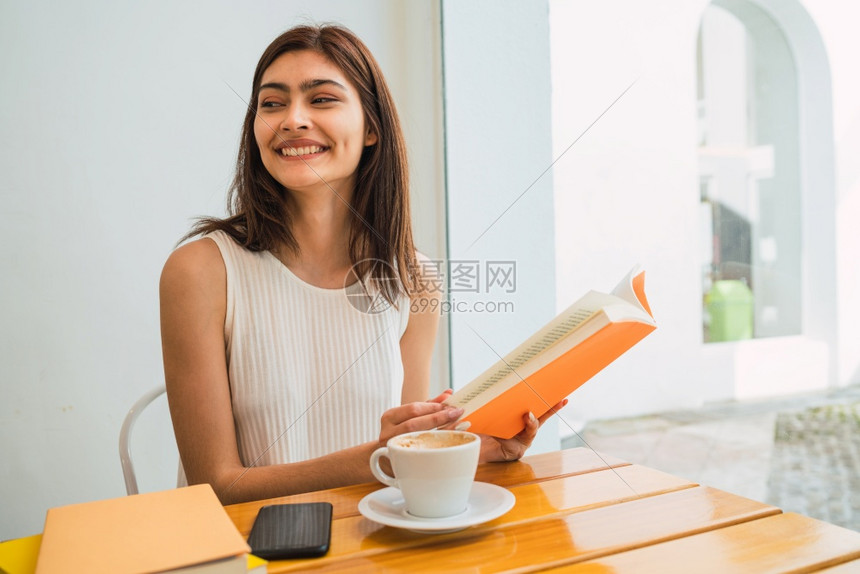 年轻女在咖啡店户外露宿时享受自由间阅读书籍图片