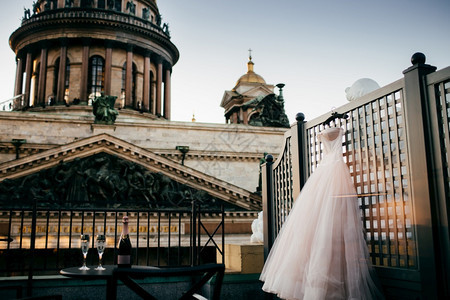 挂在衣架上的美丽白色婚纱香槟和桌子上的两个空眼镜婚礼准备与教堂背景对比的婚礼配件新娘优雅的礼服婚概念图片
