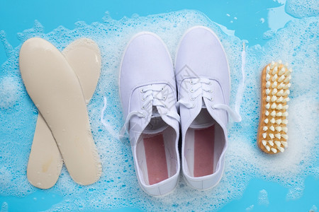 装有粉末洗涤水溶解泡沫的运动鞋和蓝底的木刷子洗脏鞋图片