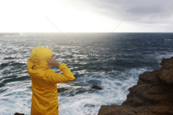 穿黄色雨衣的女子站在悬崖上仰望大海图片