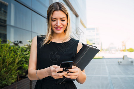 年轻商业妇女站在办公楼外时使用手机的肖像商业与成功概念图片