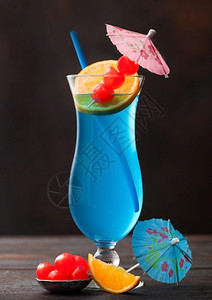 蓝环礁夏季鸡尾酒经典玻璃甜鸡尾酒樱桃和橙色切片雨伞在黑桌背景图片