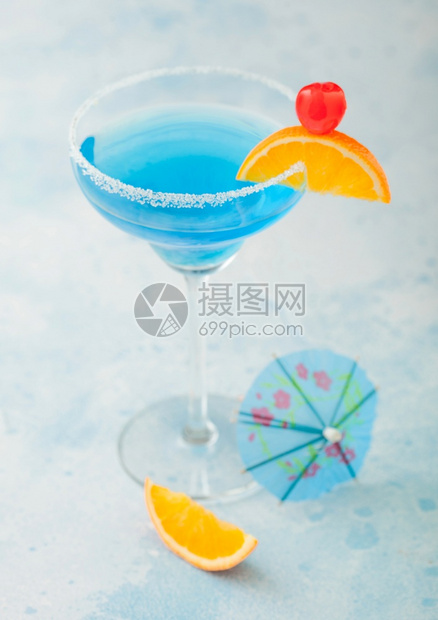 在玛格丽塔杯中有甜鸡尾酒樱桃和橙色切片蓝桌底有伞图片