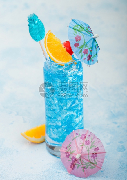 蓝色环礁湖夏季鸡尾酒在高球玻璃甜鸡尾酒樱桃和橙色切片雨伞在蓝桌背景图片