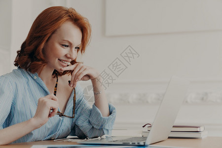 喜悦的女模式在工作空间装扮持有眼镜微笑积极使用无线互联网连接阅读信息拥有在线通信努力创建网络项目图片