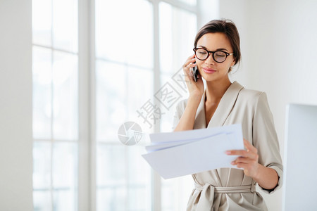 商业女人横向拍摄的镜头讨论合同细节办公室工作集中会计信息电话交谈时持有纸质文件正式穿衣图片