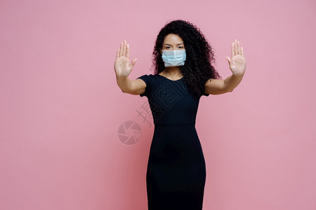 严肃的非洲女形象将手掌拉向相机做出停止的手势拒绝信号预防冠状或传染戴一次面罩与粉红色背景隔绝图片