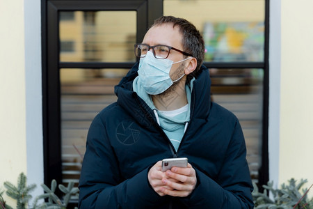 在户外拍摄的穿戴防护面罩止街上出现冠状持有手机阅读新闻关心健康使用无线互联网图片