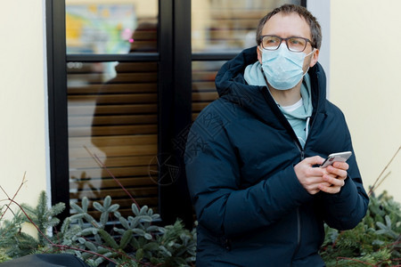 欧洲青年男子在城市街道上行走持有移动电话阅读有关冠状症的信息有在线通户外张贴保健安全概念图片