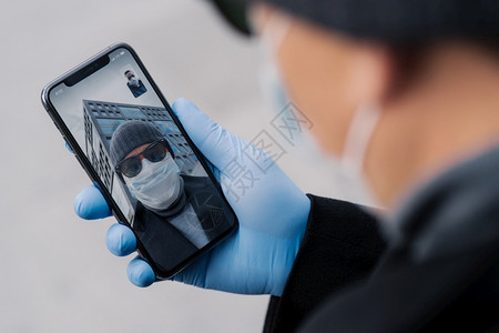 通过现代智能手机举行电视会议拍摄人的照片在科罗纳传播期间与人保持距离在公共场所户外散步时戴防护面具和橡胶手套图片