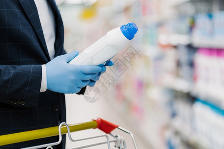 男在家用商品店中选择洗涤剂持有装液体粉的瓶子佩戴医疗手套以免受冠状的侵袭阅读产品信息背景图片