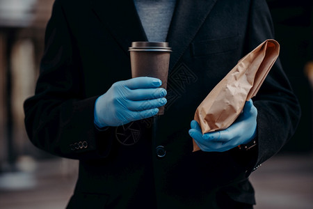 在冠状和检疫期间提供服务无脸商人扣留食物和一次咖啡佩戴医用橡胶手套以保障安全大流行病期间的营养图片