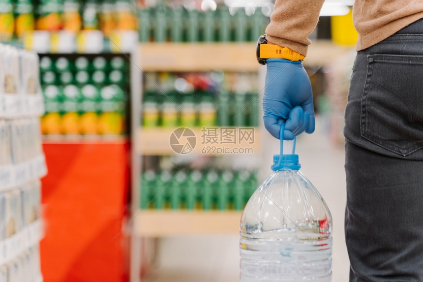 在科罗纳流行期间进恐慌购物无法辨认的直升机佩戴橡胶手套携带一瓶饮用水在超市制造爆发期间采取预防措施图片