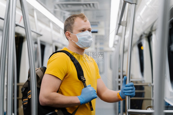 欧裔男子戴外科面具在地铁或下通勤背包保护自己免受或流行的侵害在空车中站立社会动荡之后图片