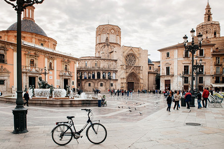 201年8月3日ValenciSpnfuetdluria喷泉自行车和游客在ValenciCthedrl广场有教堂和钟楼背景图片