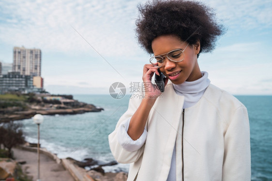 年轻美丽的拉丁女人肖像在电话室外与海对讲背景图片