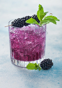 清凉的夏季鸡尾酒黑莓装在晶玻璃中冰块和薄荷装在蓝色背景上苏打汽水和酒精混合图片