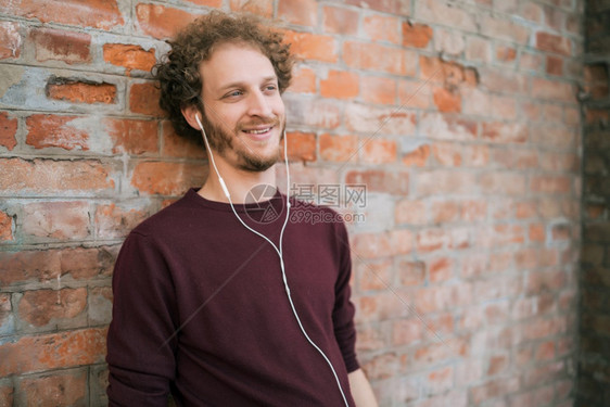 年轻人用耳机和砖墙对着听音乐的肖像城市概念图片