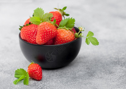 光桌背景的黑陶瓷碗叶子有机新鲜生草莓图片