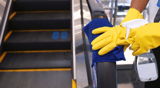 工作人员在百货商店清洁扶梯手铁以防止大流行共食19和冠状保健和卫生概念的传播图片