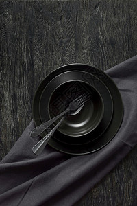 从不同的瓷器板上配有黑色餐具勺子叉毛巾或餐颜色背景相同复制空间顶部视图餐桌配有黑色炊具陶瓷板勺子和纺织品餐巾图片
