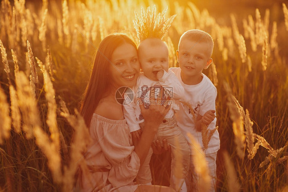 快乐的妈和两个儿子在日落时田野里快乐的童年一个轻的女人拥抱她儿子一个年轻的女人拥抱她儿子图片