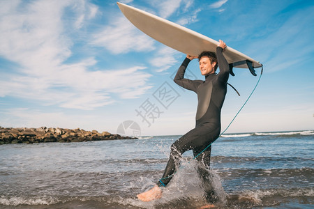 年轻冲浪者穿着黑色服带着板进入水中运动和的概念图片