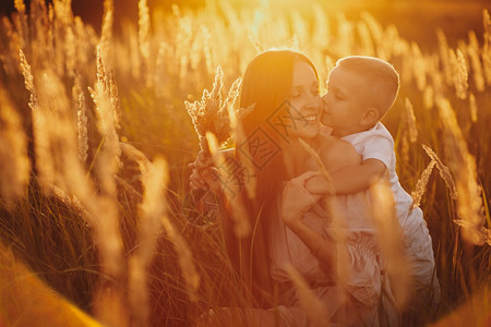 快乐的妈和儿子在田里日落快乐的童年一位轻女拥抱她的儿子图片