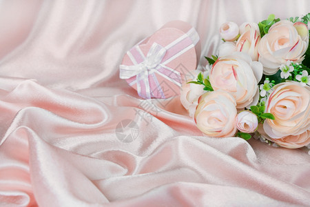 粉红骆驼花和两个心形的礼物盒在粉红丝织物背景上用白弓和粉红丝织物并有复制空间图片