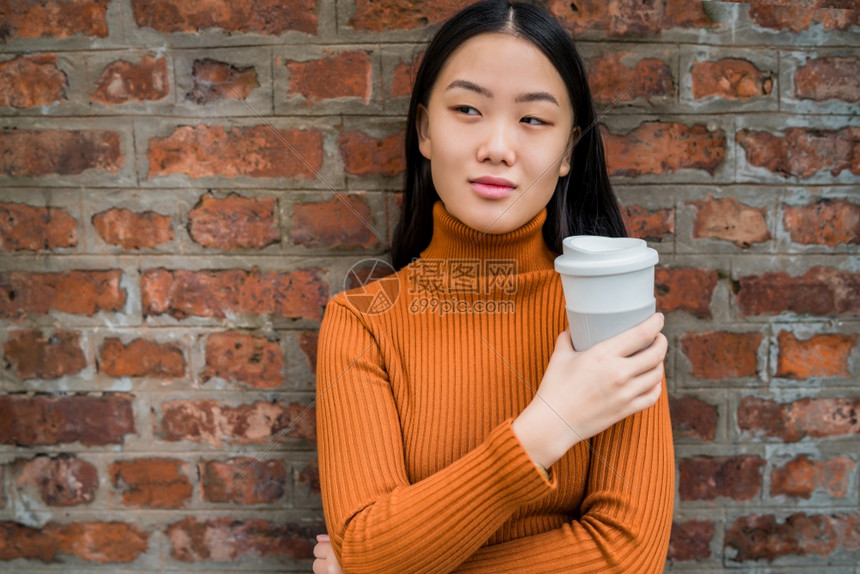年轻亚洲女在砖墙上举杯咖啡的肖像城市概念图片