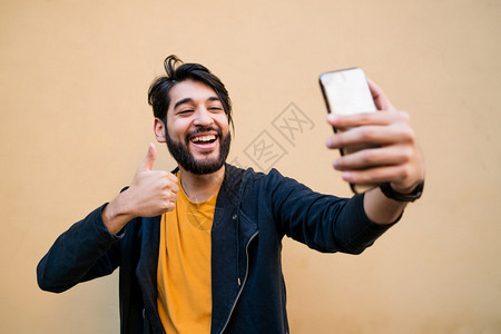 具有吸引力的年轻人用摩菲利手机和黄色墙对着拍自的肖像技术概念图片