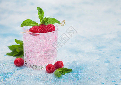 清凉的夏季粉红色柠檬水鸡尾酒在晶玻璃中装有草莓冰和薄荷放在浅蓝色背景上图片