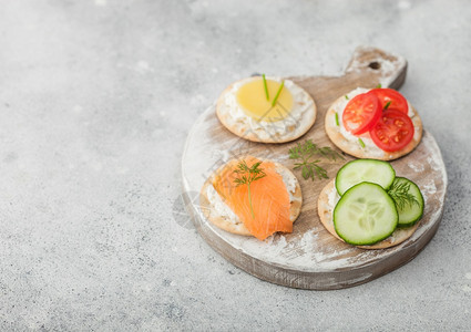 各种圆形健康饼干配有鲑鱼和奶酪番茄黄瓜放在浅色桌底的木切面板上图片
