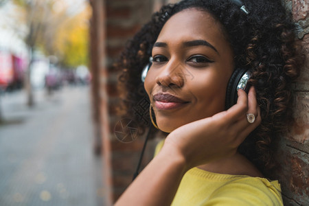 年轻美国女在街上用耳机收听音乐的肖像图片