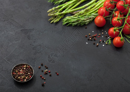 黑色食物背景健康有机食草樱桃西红柿黑桌背景的迷迭香加上一碗胡椒图片